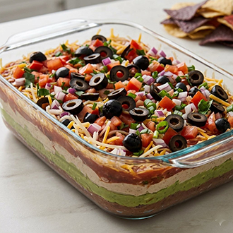 Easy 7-layer dip featuring layers of refried beans, guacamole, sour cream, salsa, and shredded cheese in a glass serving dish.