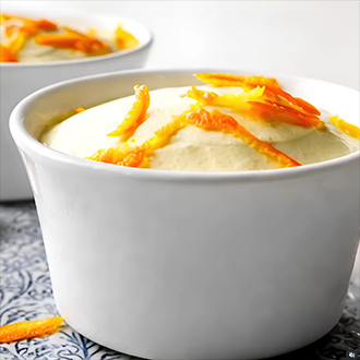 A tall Grand Marnier frozen soufflé in a ramekin with the parchment paper collar removed, garnished with fresh orange zest and berries