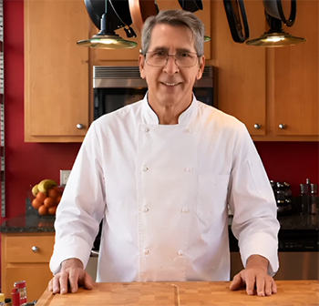 Retired Chef Dogan smiling in his home kitchen wearing a white chef uniform