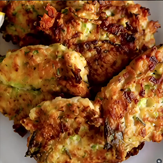 A stack of crispy Greek zucchini fritters garnished with fresh dill and crumbled feta cheese, served with a side of creamy tzatziki sauce