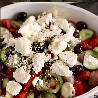 A traditional Greek salad with tomato wedges, striped cucumber slices, green pepper rings, Kalamata olives, and large slabs of feta cheese