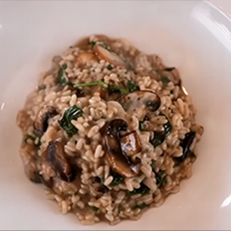 A close-up of creamy, golden-brown mushroom risotto garnished with sliced sautéed wild mushrooms, freshly grated parmesan cheese, and chopped parsley